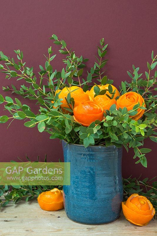 Têtes de fleurs en peau d'orange, accompagnées d'eucalyptus dans un vase bleu