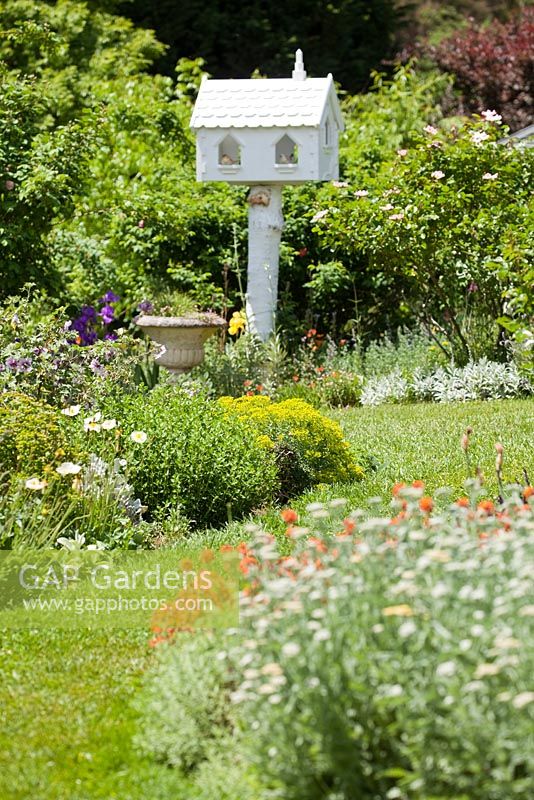 Jardin de style cottage anglais avec chemin d'herbe, parterres de fleurs herbacées et pigeonnier blanc sur colonne