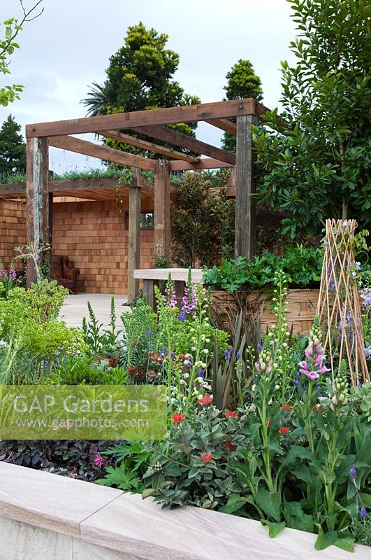Parterre de jardin surélevé donnant sur une pergola en bois recyclé, salle à manger aux murs recouverts de bardeaux de cèdre.