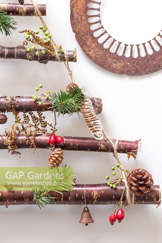 Un sapin de Noël suspendu fait de branches de bouleau. Les décorations comportent des pommes de pin, des plumes, des cynorrhodons et des têtes de graines de lierre