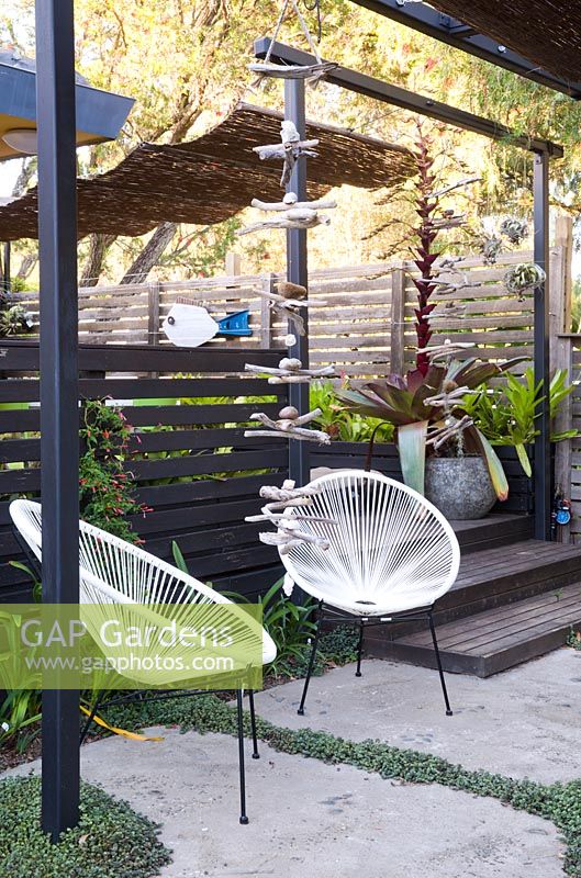 Coin salon sous verrière ombragée avec chaises acapulco blanches et mobile en bois flotté.