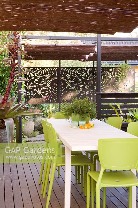 Terrasse en bois avec salle à manger informelle et écran en bois décoratif en arrière-plan. Table avec rhipsalis en pot. Alcantarea en pot vu à gauche