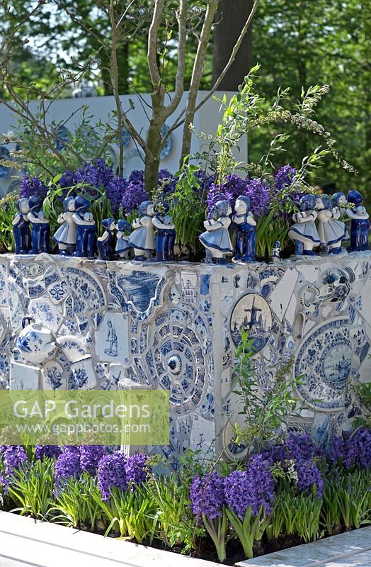 Figures hollandaises typiques en céramique Delfts Blue s'embrassant et placées sur le bord du bac à fleurs décoré rempli de Hyacinthus bleu. Jardin d'inspiration: Delfts Blue.