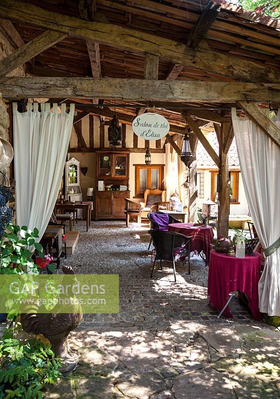 Maison et terrasse partiellement couverte en pavé uni avec salon de jardin et mobilier brocante - juillet, Les Jardins de la Poterie Hillen
