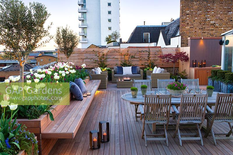Table à manger et chaises et coin salon sur une terrasse sur le toit de Londres au crépuscule avec des bougies. Avril.