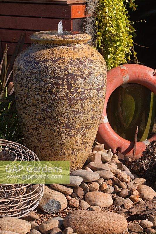 Section d'un jardin utilisant une collection d'éléments rustiques, un anneau de sauvetage, un pot Atlantis comme eau avec une succulente rampante, des Dischidia et un pot de homard