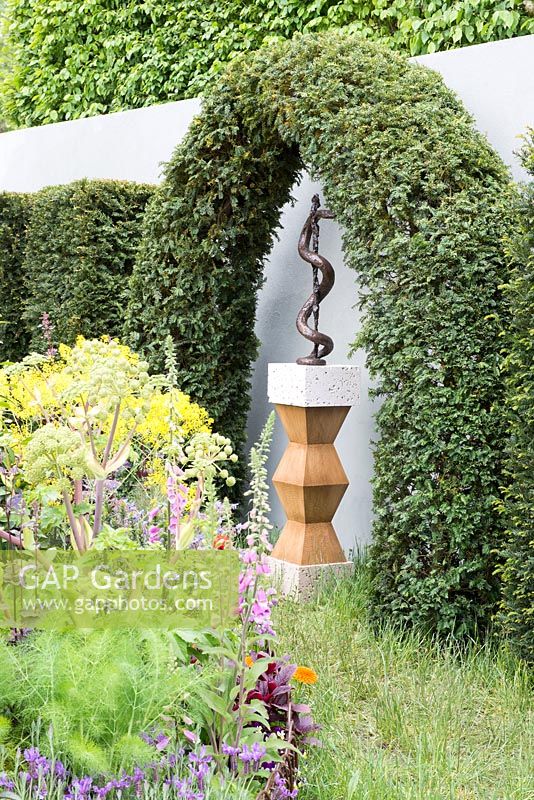 Sculpture du personnel d'Asclepius par Susan Bacon sous une arche de Taxus baccata, Angelica archangelica en premier plan - Un apothicaire moderne, Le jardin de l'hospice de St John, RHS Chelsea Flower Show 2016. Concepteur: Jekka McVicar, parrain: St John's Hospice