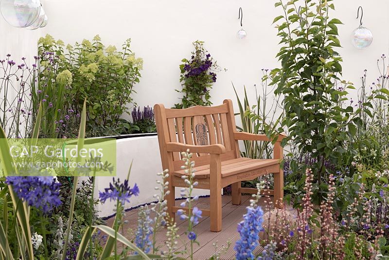 Un patio aux murs blancs, des parterres de fleurs surélevés avec des vivaces bleues, violettes et vert lime et un banc en bois naturel. Une bouffée d'air frais, RHS Tatton Flower Show 2011, Cheshire
