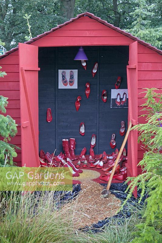 Un hangar peint en rouge plein de chaussures rouges dans un cadre boisé. Conte de fées, RHS Tatton Flower Show 2011, Cheshire