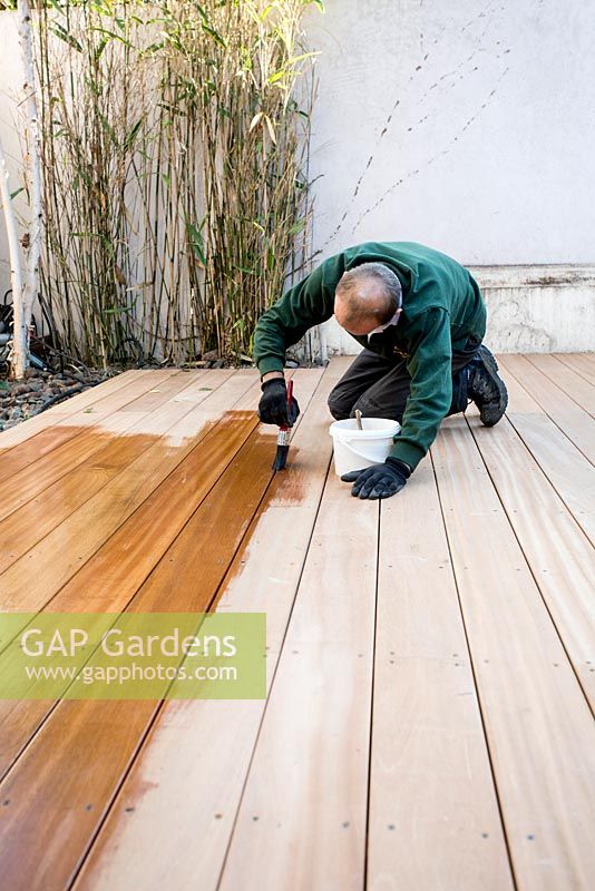 Application d'huile de bois au platelage de bois fini dans un petit jardin urbain