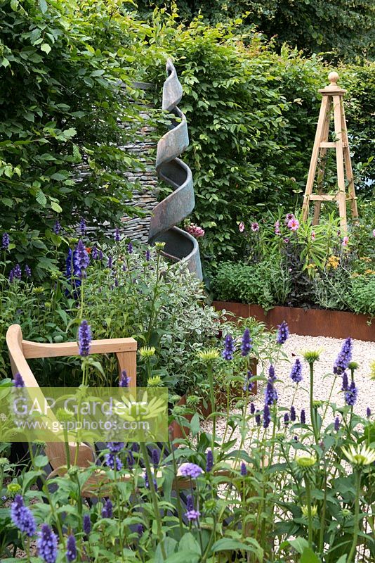 Un jardin inspiré des arts et de l'artisanat avec un banc fait à la main, un obélisque et une sculpture en spirale. Une retraite d'été conçue par Laura Arison et Amanda Waring. RHS Hampton Court Flower Show 2016