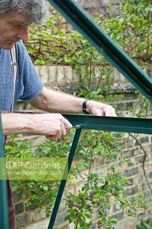 Homme remontant le cadre en aluminium de la serre à l'aide d'un tourne-écrou hexagonal de 10 mm. Avril, printemps.