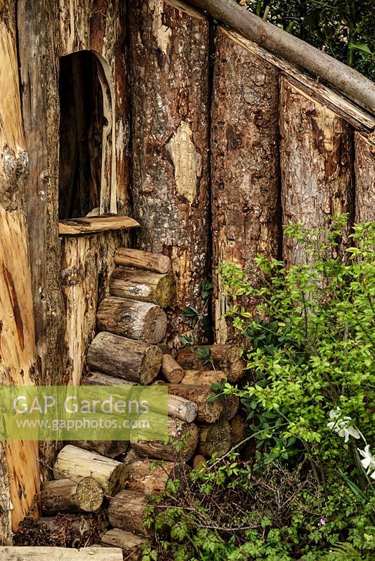 Bord d'une cabane en bois rustique avec pile de bûches empilées - Le jardin du bûcheron - RHS Malvern Spring Show 2016. Concepteur: Mark Walker, commanditaire: Howards Motors
