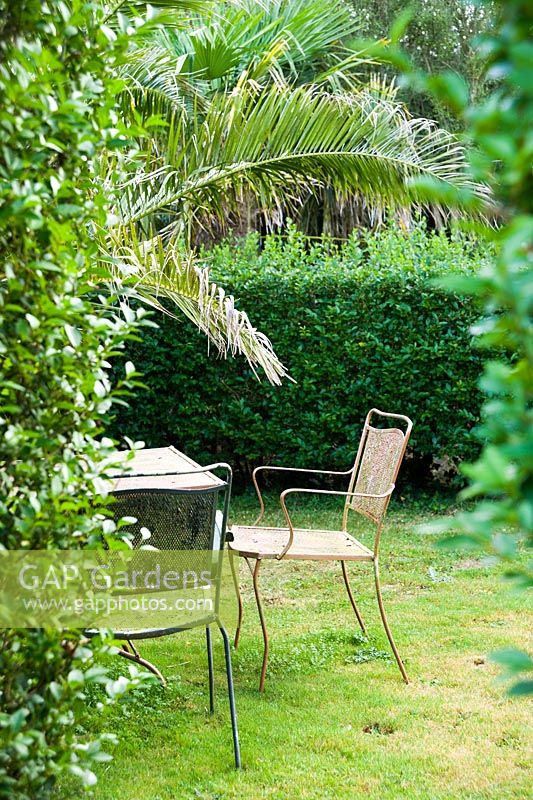 Table et chaises en métal à l'intérieur d'une des 'chambres privées' du jardin qui protègent des vents dominants