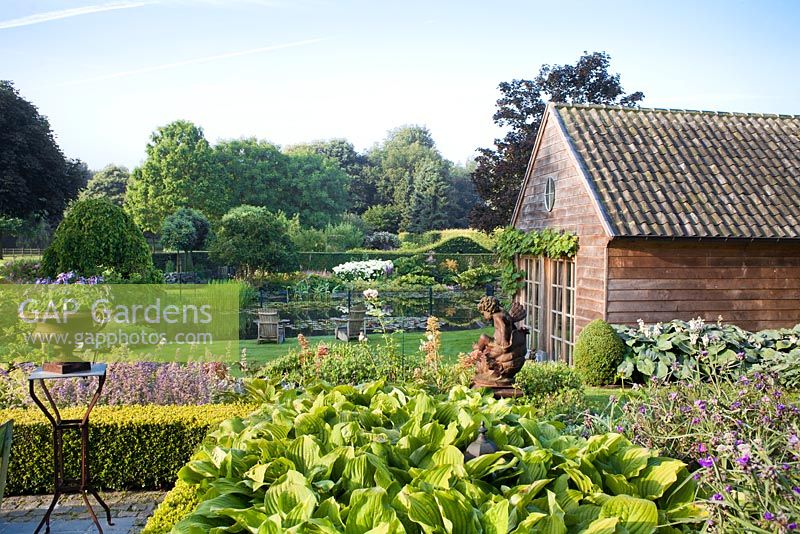 Vue depuis la terrasse: parterre de vivaces, statue d'ange enfant, jardin et urne décorative. Jardin Yvan et Gert En Belgique.