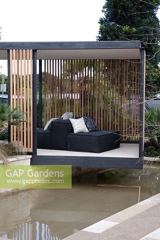 Un pavillon de jardin à charpente en acier noir se dresse au-dessus d'un plan d'eau, avec une latte en bois de cèdre