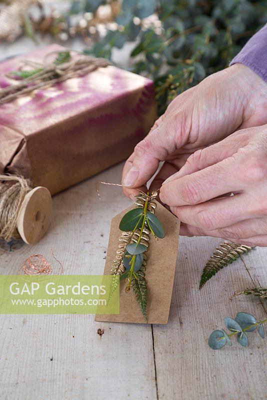 Création d'une étiquette cadeau naturelle en combinant des feuilles d'eucalyptus et de fougère peinte à l'or