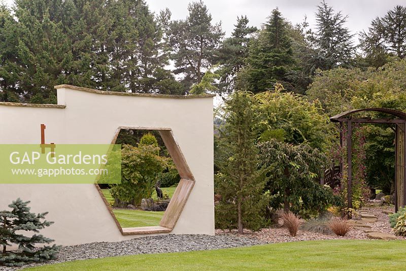 Vue à travers une ouverture hexagonale dans un mur caractéristique vers le jardin au-delà. Jardin de style japonais, juin. Yorkshire du Nord.