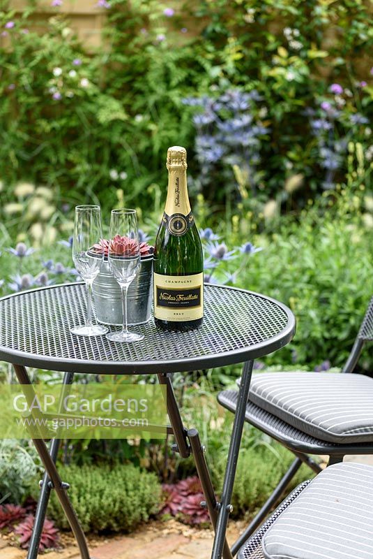 Une table et des chaises de bistrot rondes en métal avec champagne et aeonium dans un pot de fleurs en métal dans le jardin de la sécheresse, RHS Hampton Court Flower Show 2016