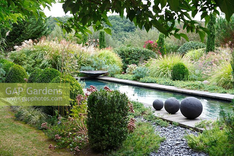Trois boules de grès sont placées au bord de la piscine du Jardin Contemporain, Les Jardins de la Poterie Hillen