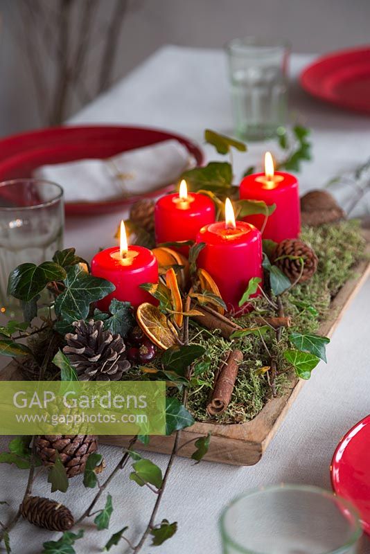 Une pièce maîtresse festive construite à partir de mousse, de pommes de pin, de bâtons de cannelle, de lierre, de tranches d'orange séchées et de bougies allumées