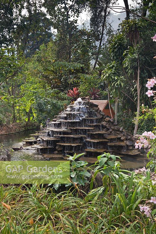 Fontaine décorative de pierres plates en gradins dans les jardins tropicaux avec maison de canard derrière - Lake Atitlan Hotel, Guatemala