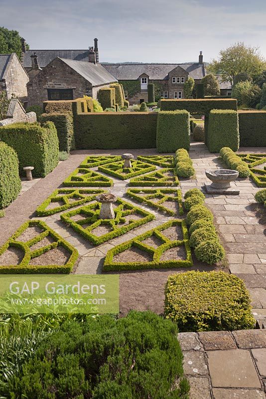 Une vue de la maison à travers le jardin de fantaisie avec son motif rose Tudor fabriqué à partir de la boîte - juin, Herterton House, Hartington, Northumberland, UK