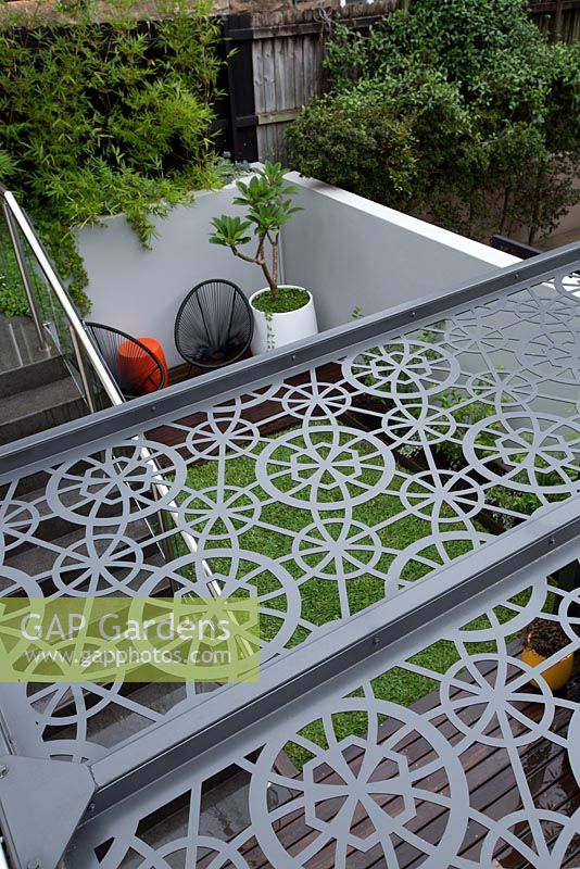 Vue de dessus d'un toit de pergola en métal gris découpé au laser montrant la terrasse en bois et le coin salon ci-dessous.