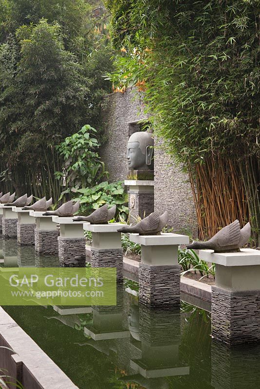 Un étang rectangulaire formel avec des sculptures d'oies sur des socles d'ardoise empilés et une grande tête de Buddah - Java, Indonésie