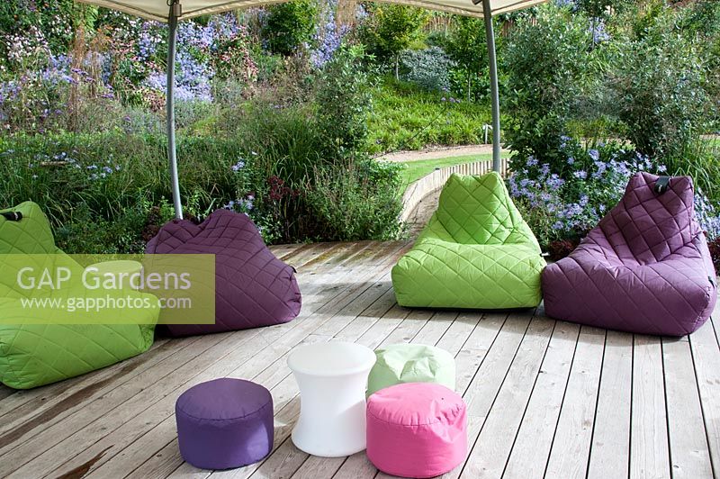 Jardin moderne avec terrasse en bois et sièges en coussin souple multicolore sous un gazebo