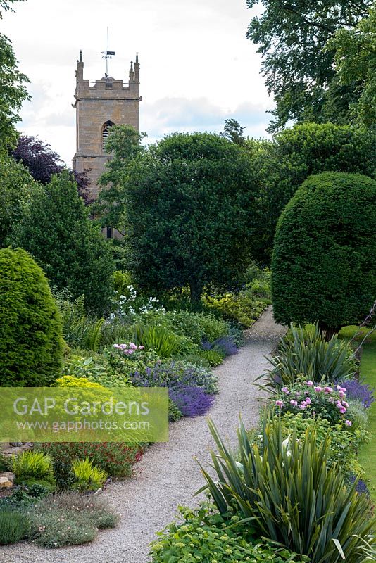 La promenade de l'église au manoir Bretforton avec de longs parterres de fleurs herbacées doubles et des ifs en forme.