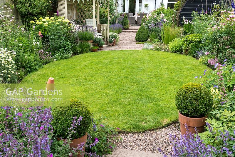 Une pelouse circulaire est entourée de parterres herbacés de style chalet de menthe des chats, géranium rustique, marguerite, scabieuse, hortensia, lavande, roses et digitales.