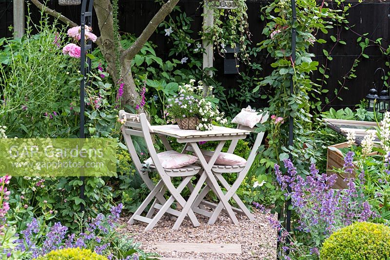 Table sur petite terrasse ombragée de pommier et bordée de menthe et de roses.