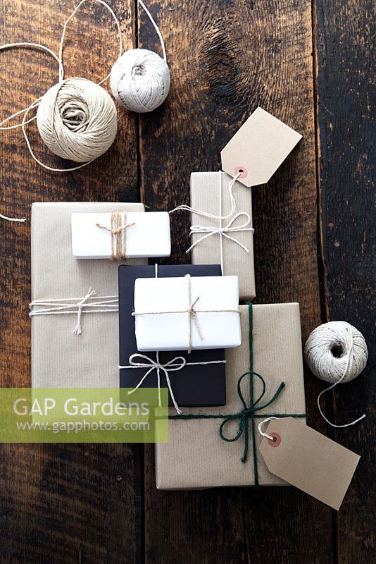 Beaucoup de cadeaux enveloppés de papier brun et blanc et attachés avec de la ficelle, avec des étiquettes-cadeaux et de la ficelle.