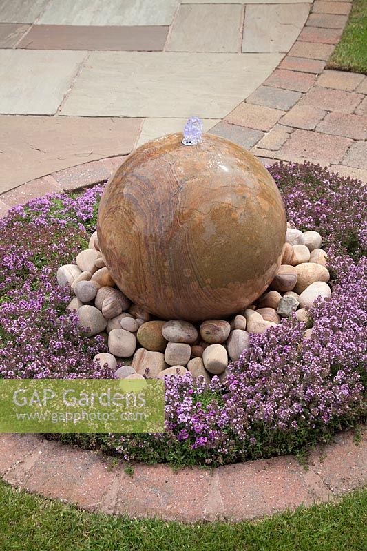 Sphère de pierre arc-en-ciel caractéristique de l'eau entourée de galets et de plantes de thymus - juin, Summerfield Place, Cheshire