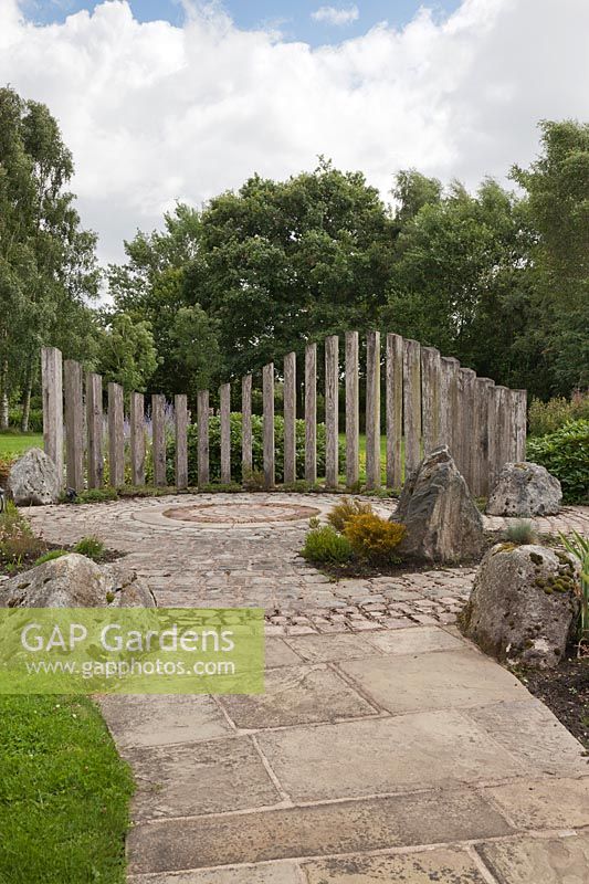 Une vue sur le jardin avec une sculpture de traverse de chemin de fer, des roches placées et une zone pavée circulaire en pierre