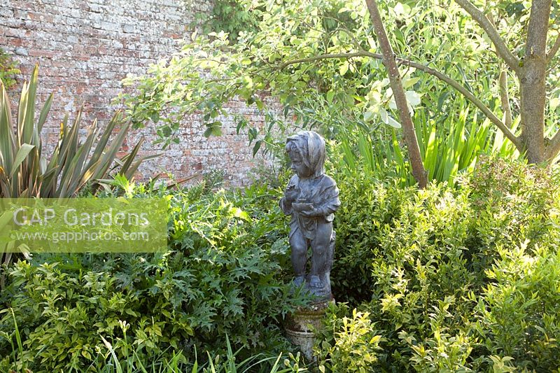 Statue décorative d'enfant parmi le feuillage mixte pour la texture dans le jardin clos