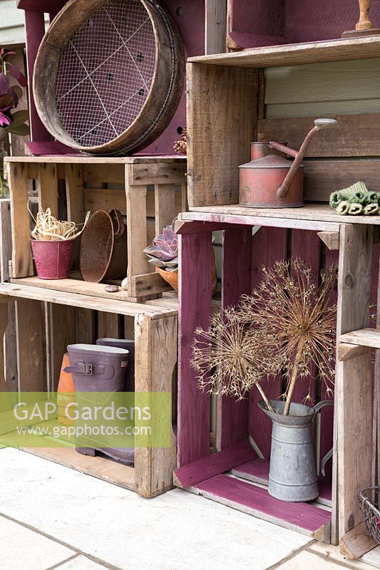 Stockage de caisses en bois vintage avec divers pots, bottes de jardin, un arrosoir rustique et des têtes de graines d'Allium