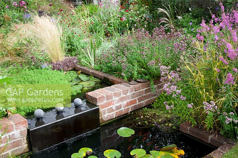 Un petit jardin de chalet moderne à faible entretien planté de vivaces auto-ensemencées. Un plan d'eau couvert de plomb comporte un étang à deux niveaux avec un feuillage de nénuphar