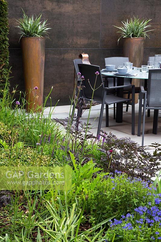 Jardin de banlieue contemporain avec mur en cuivre, pots et coin salon