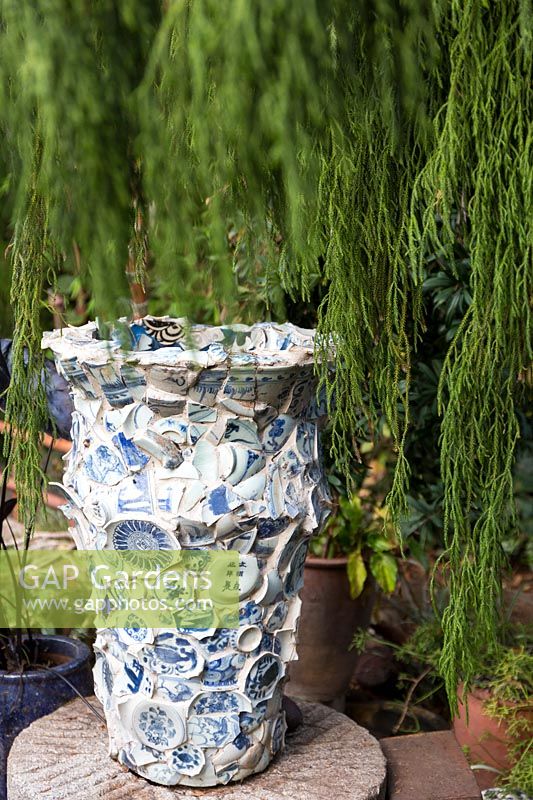 Grande urne face à des morceaux de porcelaine bleue et blanche brisée entourée d'un genévrier pleureur. Jardin du sculpteur et céramiste Marcia Donahue à Berkeley, Californie.