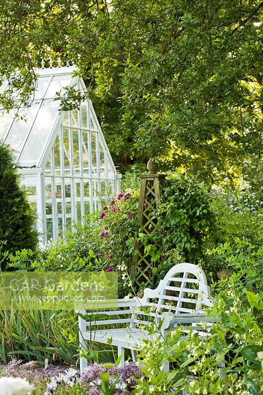 Endroit isolé avec banc de jardin sous un chêne anglais mature, obélisque comme support de roses et de clématites soutenu par une véranda. Création: Carol Bruce