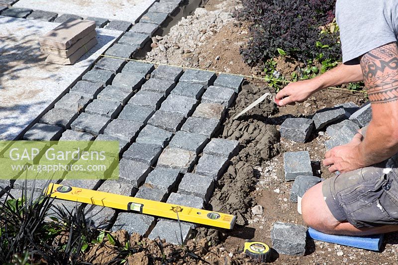 Faire un patio en matériaux mixtes - l'homme prépare le parterre de mortier pour les pavés de granit pour le chemin menant au patio