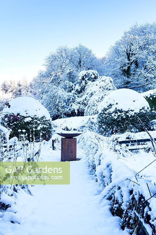 Le jardin avant avec bain d'oiseau sur colonne de chêne dans la neige. Veddw House Garden, Monmouthshire, Pays de Galles, Royaume-Uni. Le jardin a été créé depuis 1987 par l'écrivain Anne Wareham et son mari, le photographe Charles Hawes. Le jardin s'ouvre régulièrement au public pendant les mois d'été.