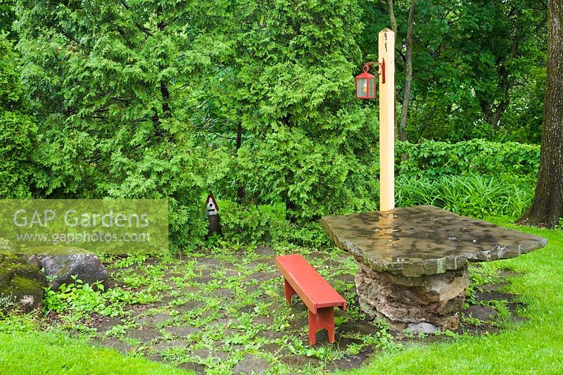 Patio dalle avec banc en bois rouge et table en dalle de pierre bordée de Thuja occidentalis - haie de cèdres dans une cour résidentielle à la fin du printemps, Québec, Canada.
