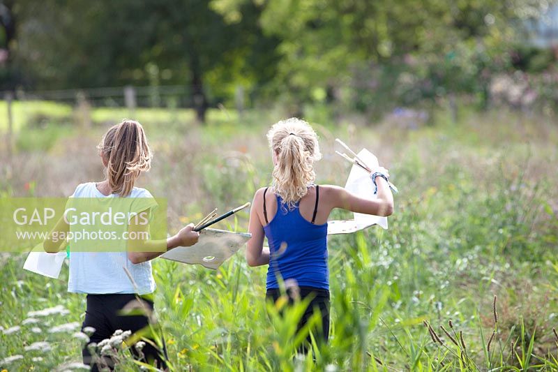 Deux filles qui courent avec des pinceaux, du papier et de la peinture. Peinture dans les champs de fleurs, août.