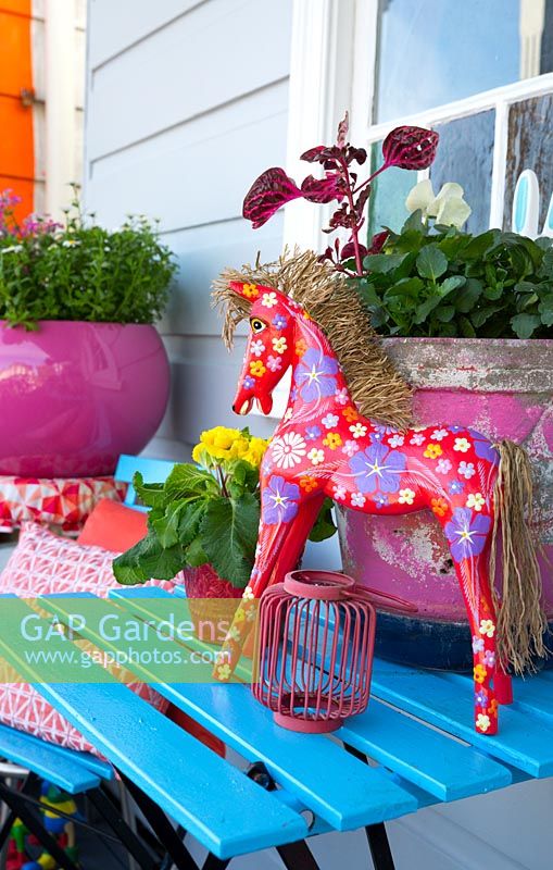 Table à lattes bleu vif avec des pots roses et un cheval rouge peint avec un motif floral, août.