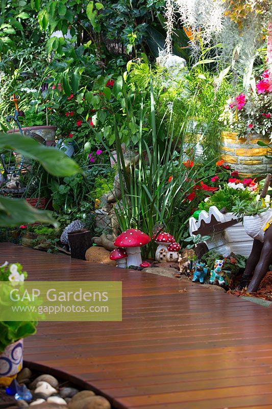 Détail d'une passerelle en bois courbé avec des plantes aimant l'ombre et une collection de jouets, de pots et d'ornements de jardin avec un groupe de fée-champignons rouges et blancs.