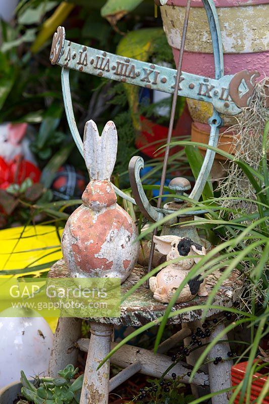 Une collection éclectique d'objets avec un gnomon de cadran solaire en bronze, un lapin en terre cuite et un cochon sur un tabouret rustique.