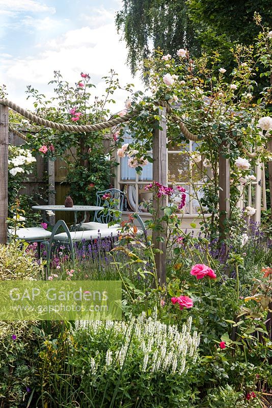Les roses sont dressées le long d'un butin de corde, entourant un patio pour se détendre près de la maison d'été.